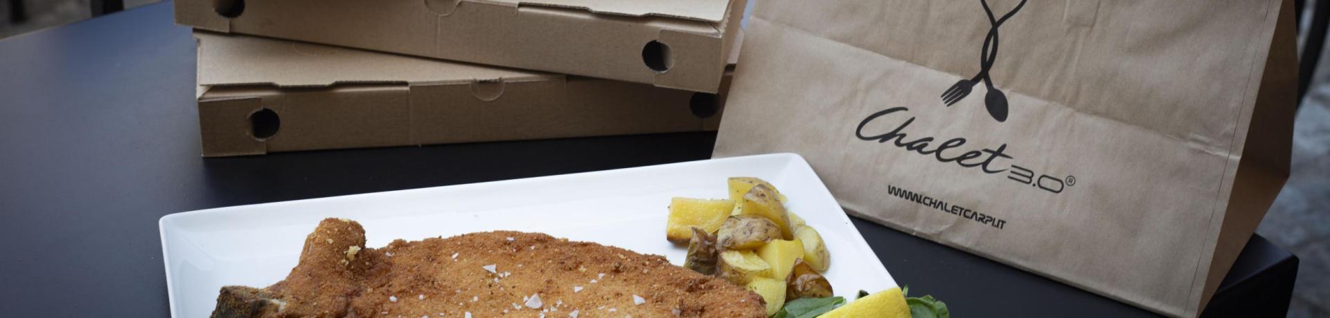 Cotoletta con patate e limone, pizza da asporto su tavolo all'aperto.